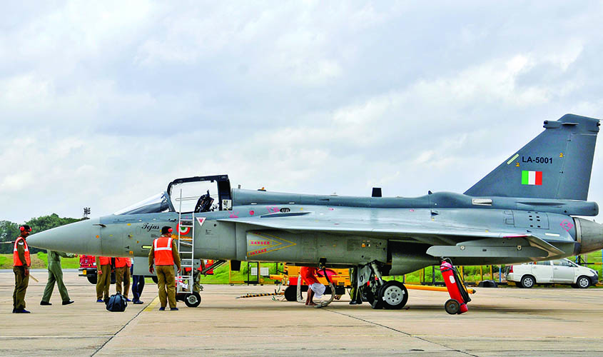 Airport ground staff stand besides Tejas, India's first locally-built LCA, before its induction into the Indian Air Force at the HAL airport in Bengaluru