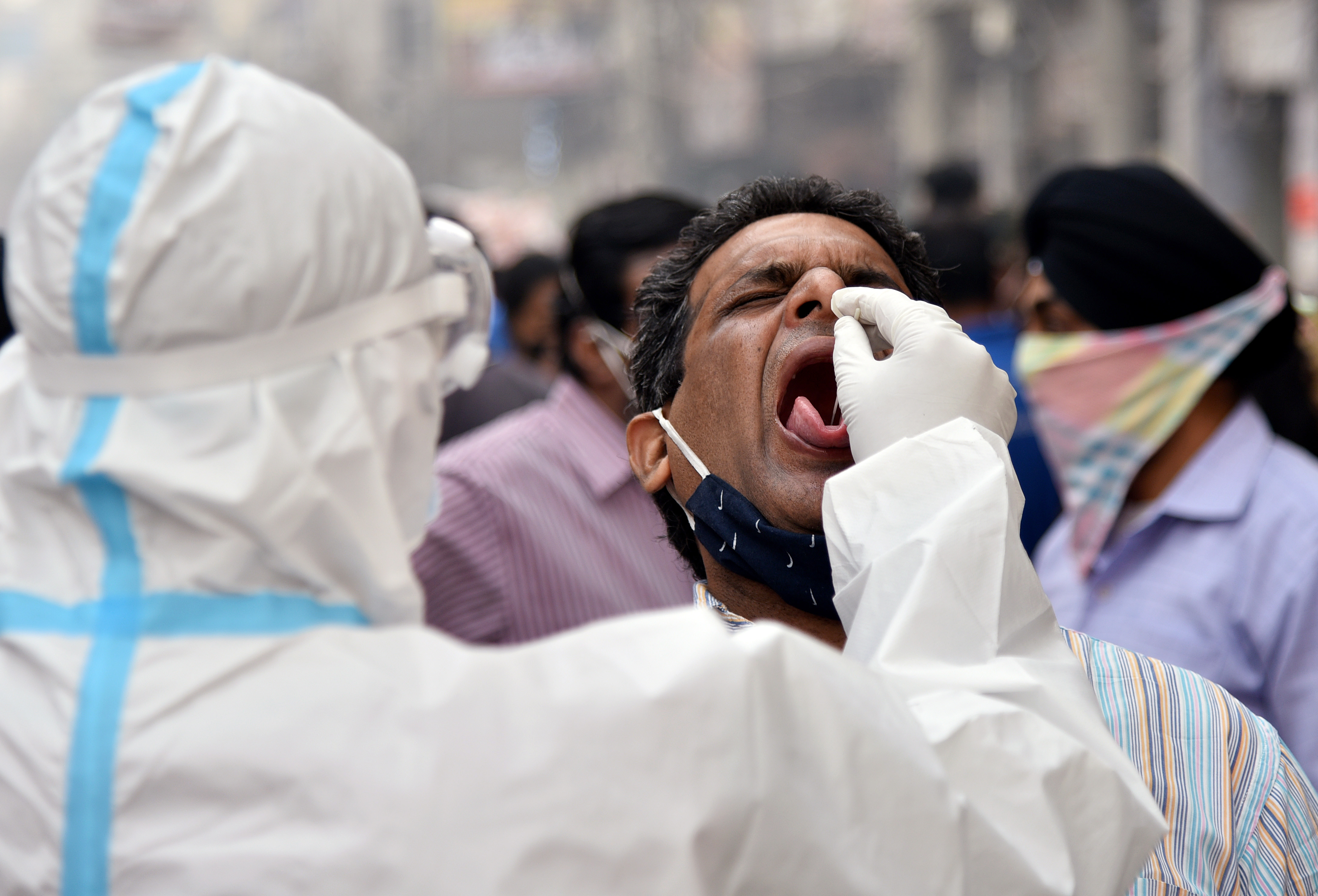 A health worker in personal protective equipment (PPE) collects a swab sample from a man
