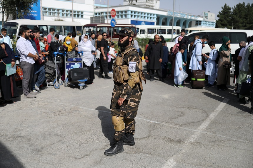 A member of Taliban security forces stands among travelers at the international airport in Kabul