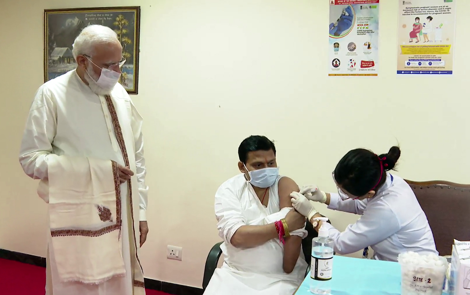 A beneficiary receives a dose of the COVID-19 vaccine in presence of PM Narendra Modi during his visit to RML Hospital
