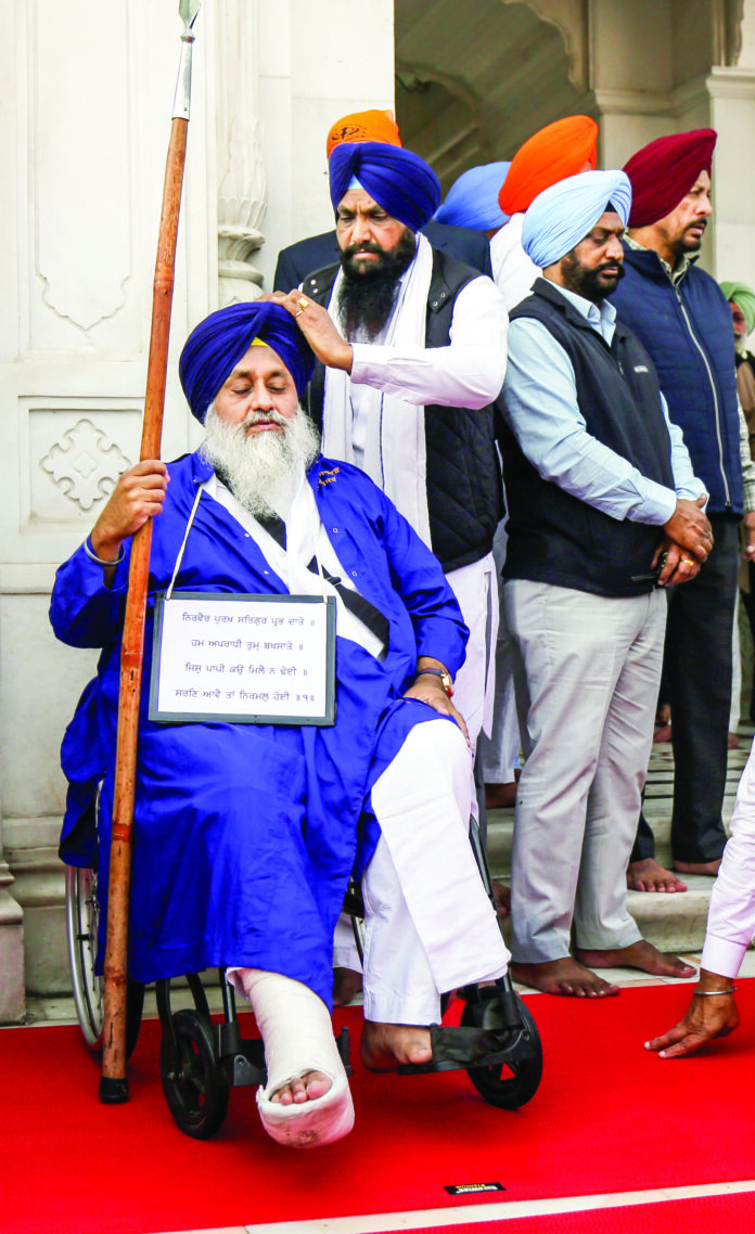 Former Punjab Deputy CM Sukhbir Singh Badal sits on a wheelchair with a plaque around his neck and performs sewadar (guard duty) following the religious punishment pronounced for him by Sri Akal Takht Sahib, at the entrance of the Golden Temple in Amritsar on Tuesday. ANI Former Punjab Deputy CM Sukhbir Singh Badal sits on a wheelchair with a plaque around his neck and performs sewadar (guard duty) following the religious punishment pronounced for him by Sri Akal Takht Sahib, at the entrance of the Golden Temple in Amritsar on Tuesday. ANI